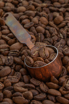 Hand-roasted Arabica Maragogipe coffee beans in a copper measuring spoon resting on top of the freshly roasted beans.
