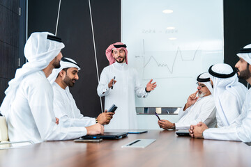 Group of corporate arab businessmen meeting in the office - Business people wearing emirati clothing  working in the office - 733263901