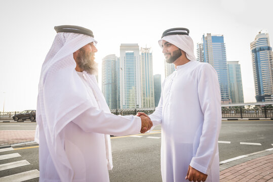 Arab businessmen wearing traditional emirati kandora meeting outdoors - Middle-eastern adults with dishdasha clothing bonding in Dubai