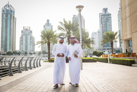 Arab businessmen wearing traditional emirati kandora meeting outdoors - Middle-eastern adults with dishdasha clothing bonding in Dubai