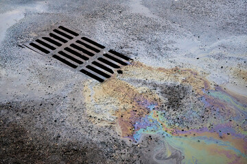An oil or gasoline slick against the backdrop of an asphalt road flows into a storm drain....