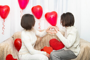 People hold their hands together with a heart symbol among the heart-shaped balloons.Valentine