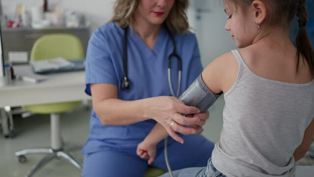 Doctor examining young girl, measuring blood pressure, using medical blood pressure monitor. Concept of preventive health care for children.