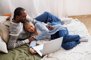 Relaxed young multiethnic couple looking at laptop on bed