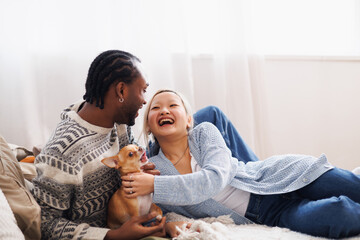 Positive young diverse couple playing with pet on bed at home