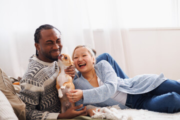Happy young multiethnic couple relaxing and playing with dog at home