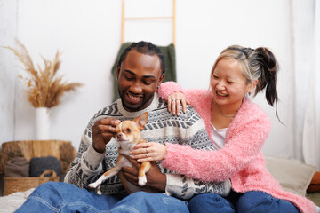 Positive young multiethnic couple spending time with pet on bed at home