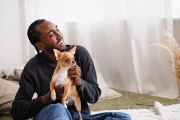 Smiling young african american man chilling with dog on bed at home