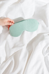 Mint color silk eye mask for sleep on bed background, minimal lifestyle aesthetic. Top view woman...