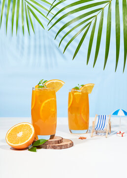 Glass of 100% Orange juice with orange slices fruits on sea beach with white sand. Summer sea vacation and travel concept. Exotic summer drinks.