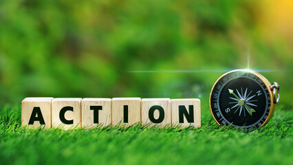 Word ACTION on wooden cubes with gold compass on green grass over blur nature background with...