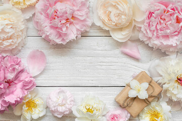Flower composition. Frame made of pasrel pink peony, white roses and jasmine flowers with gift box on white wooden background. Flat lay. Top view. Womens day, Wedding or anniversary card