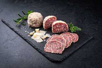 Traditional Italian saltufo salami with parmesan coated and truffle served as close-up on a black design tray