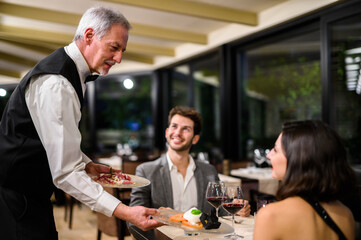 Senior waiter serving young couple at elegant restaurant