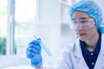 Closeup female woman scientist's hand holding blue liquid chemical chemistry test tube working in...