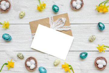 Fototapeta na wymiar Easter greeting card in frame made of spring yellow Narcissus flowers and easter colorful eggs on white wooden background. Flat lay. Mock up. Top view with copy space