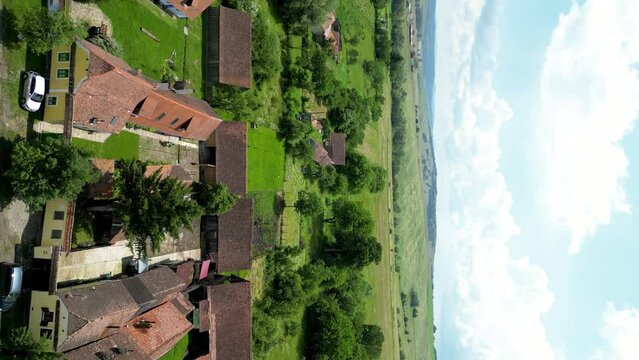 Vertical video of Viscri Village. Drone tracking right above the village. Beautiful traditional houses. Famous travel destination in Brasov, Romania. Countryside of Romania. Green, natural landscape.