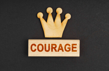 On a black surface there is a wooden crown and a block with the inscription - Courage