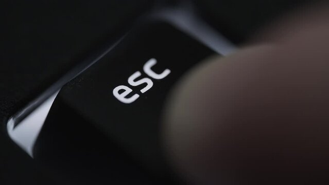 Pressing and holding escape key on black computer keyboard. Close up. 
