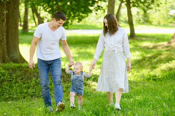 Happy married couple walks with a child in the park, holding hands, surrounded by green plants, enjoying relaxation in nature. Motherhood, childhood, fatherhood. Solitude with nature