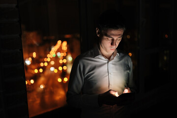 Successful businessman using holding smartphone phone, texting, typing and reading social media apps, notification and message online working late, standing on office balcony in busy town, bokeh light