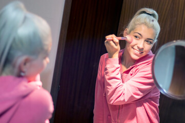 Blonde beautiful woman doing makeup in front of mirror