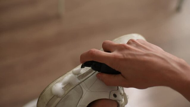 Top view of unrecognizable man applying cleaning foam to dirty light-colored soles of white sneakers. Process cleaning white trendy sneakers from dirt and dust. Concept of caring for leather footwear