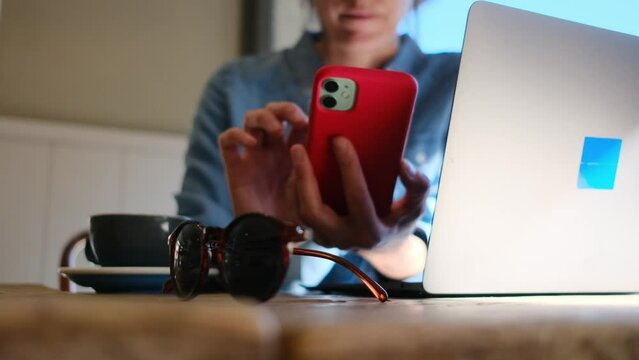 In a vibrant cafe setting, a confident Hispanic businesswoman seamlessly balances work on her laptop and phone, embodying the vigor and versatility of contemporary entrepreneurship