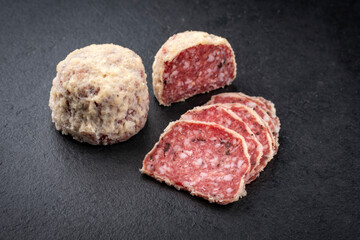 Traditional Italian saltufo salami with parmesan coated and truffle served as close-up on a black design tray