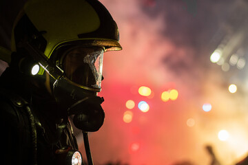 Close-up of a firefighter wearing a helmet and breathing apparatus mask at a night fire with blue and red lights in the background