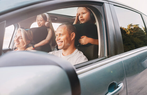 Happy smiling young couple with two daughters inside car during auto trop. They are smiling, and laughing during a road trip. Family values, tatraveling, automotive industry concept.