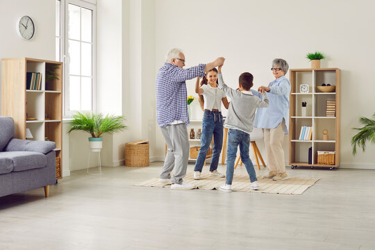 Family having fun at home. Joyful children and grandparents spend free time together. Cheerful, happy grandmother, grandfather and little kids dancing in a circle in a big, light, spacious living room