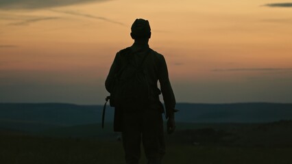 Silhouette of lonely soldier walking in field on red sunset background. A sad conceptual scene...