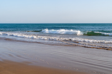 A small wave crash on the sandy beach, sunny