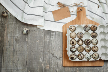 A background with cardboard packaging of quail eggs, board and cloth on the table. The concept of healthy natural organic nutrition with label mock up. Top view. Copy space.