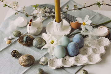Stylish easter eggs in tray, cherry blossom and candle on rustic table. Happy Easter! Modern natural dyed marble eggs and spring flowers. Festive rural still life