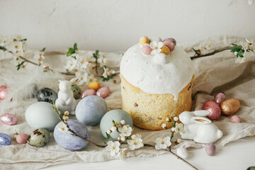 Obraz na płótnie Canvas Stylish easter eggs, panettone, bunnies, cherry blossom composition on rustic table. Happy Easter! Modern natural dyed eggs, festive food and spring flowers. Rural still life