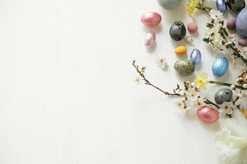Stylish easter eggs and cherry blossom flat lay on rustic white table. Happy Easter! Modern natural dyed and chocolate eggs with spring flowers. Festive template with copy space