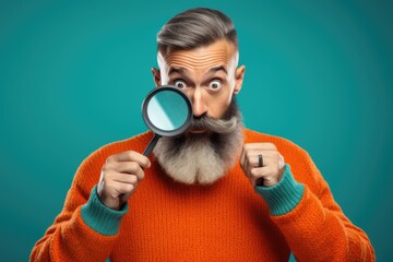 Man in orange sweater investigates with magnifying glass - obrazy, fototapety, plakaty