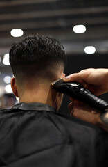 peluquero profesional cortando el pelo con maquina a un cliente - obrazy, fototapety, plakaty