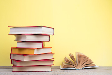 Composition with hardback books, fanned pages on wooden deck table and yellow background. Books stacking. Back to school. Copy Space. Education background.