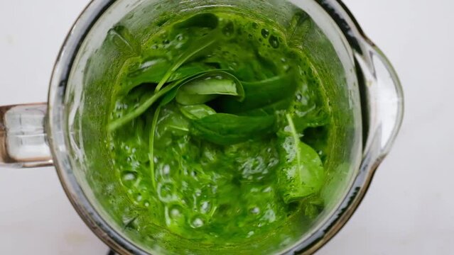 Cooking spinach smoothie in blender. Green vegetable leaves blended in blender. Slow motion. Healthy detox drink concept. Top view