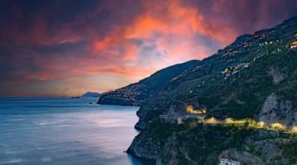 Selbstklebende Fototapeten Amalfi Coast, Italy. View over Praiano on the Amalfi Coast at sunset. Street and house lights at dusk. In the distance the island of Capri on the horizon. Amalfi Coast road. Sea landscape. © Alessandro