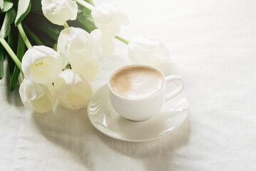 Cozy morning coffee cup with white tulip flowers from above, breakfast on Mothers day or Women's day. Top view with copy space Floral composition Romantic background