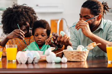 Happy multicultural family is painting easter eggs at home together.