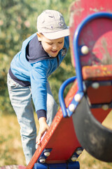 A little boy balances climbing up a red swings board.