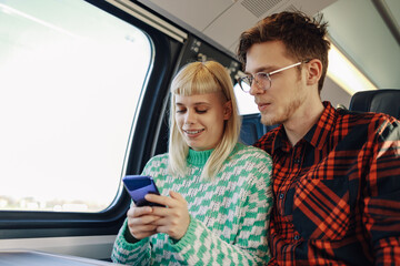 A couple is sitting in a train and buying tickets online on the phone.