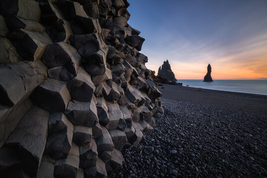 Reynisdrandar basalt sea stacks on the black sand Reynisfjara beach in Iceland with basalt rock formation in the foreground