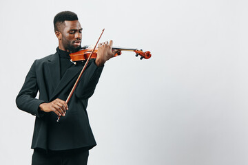 Talented young African American man in stylish black suit playing violin with passion, isolated on...