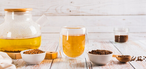 Fresh buckwheat tea in a glass, teapot and granules in a bowl on the table  web banner